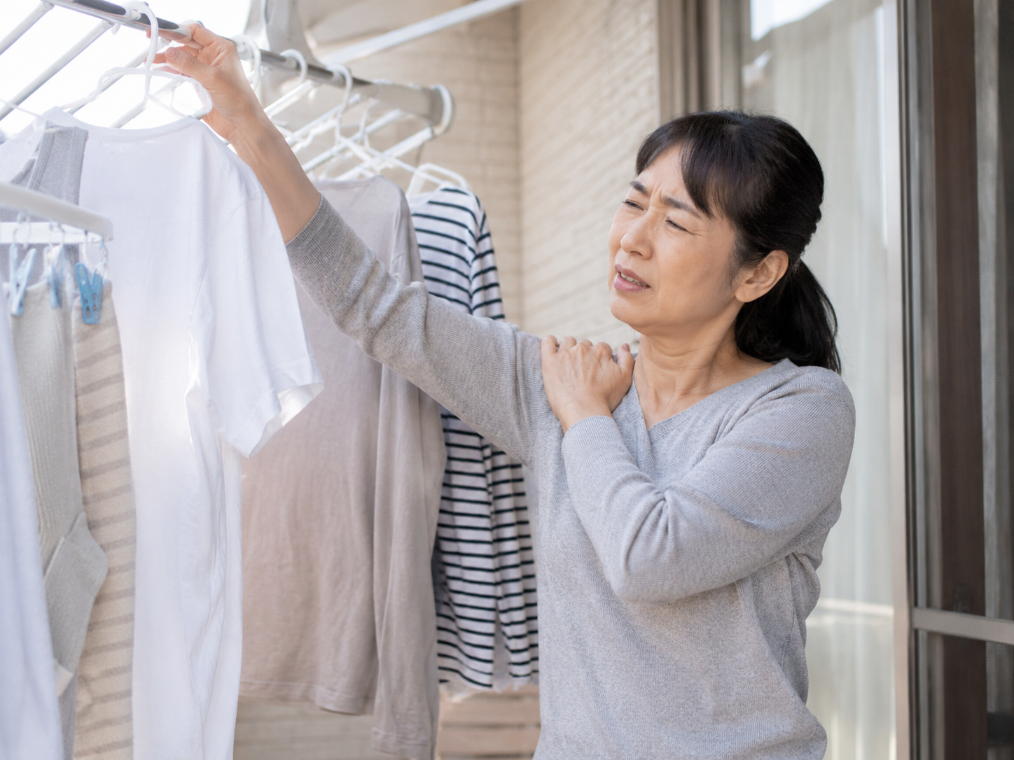 洗濯物を干す時に腕を上げて肩の痛みを感じている40代女性