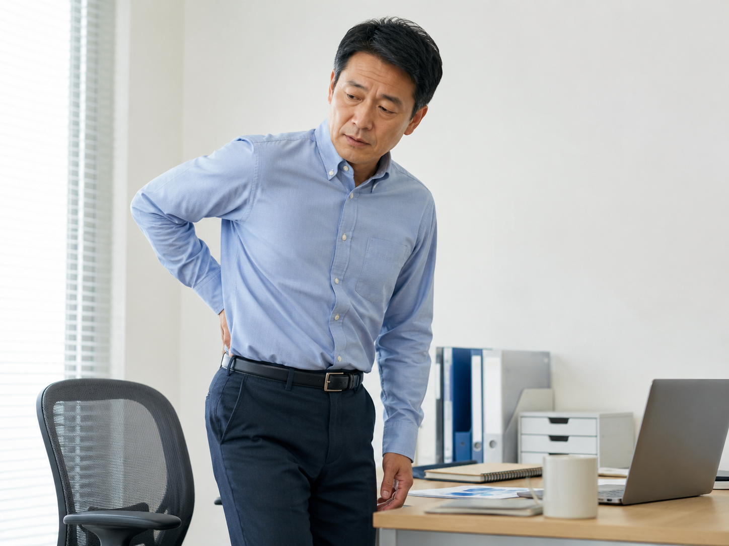 長く座ったあとに立ち上がり腰の重さを感じている男性